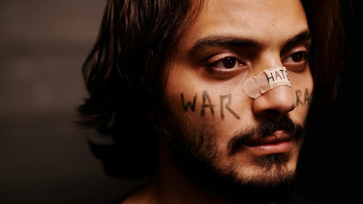 Close-up portrait of a man with 'war' and 'hate' messages on face in conceptual art.