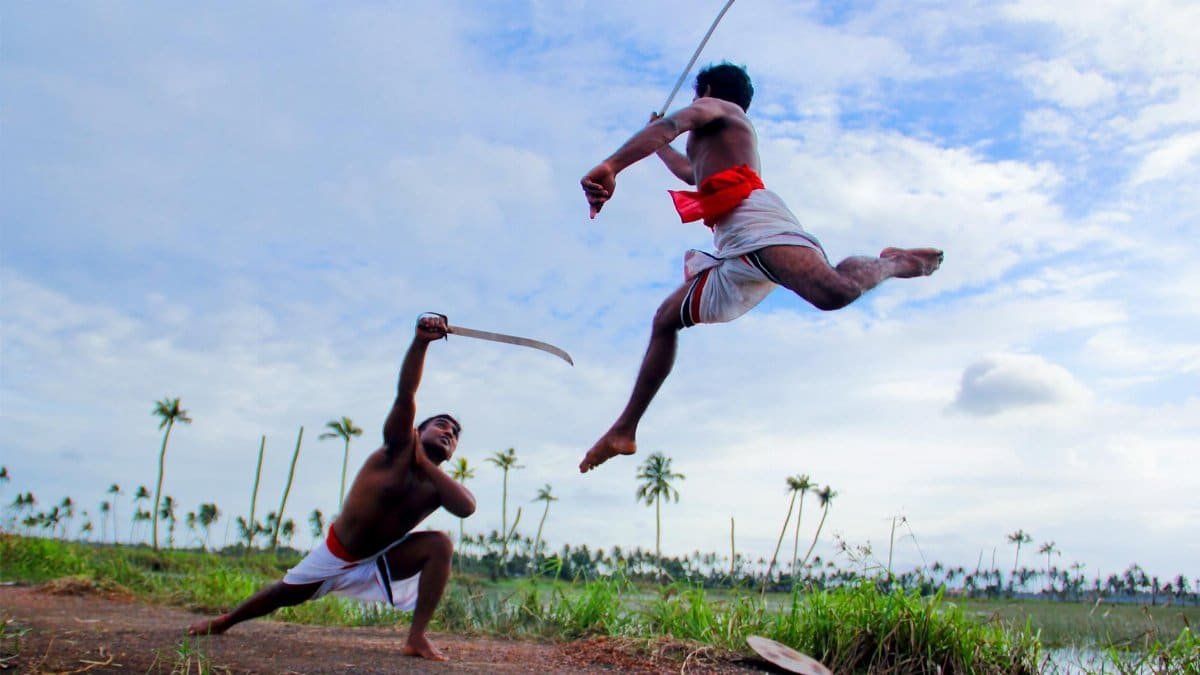 Two men perform Kalaripayattu, an Indian martial art, outdoors in Kottayam.