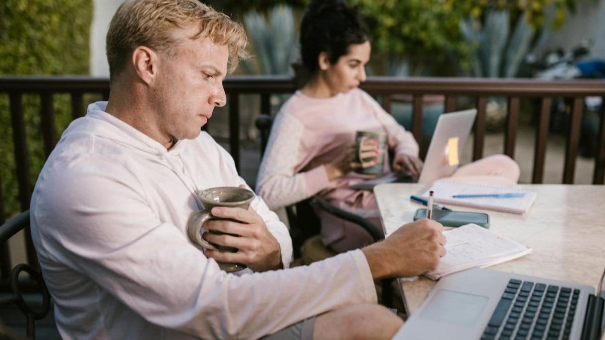 A couple working together on their laptops while enjoying a coffee outdoors.