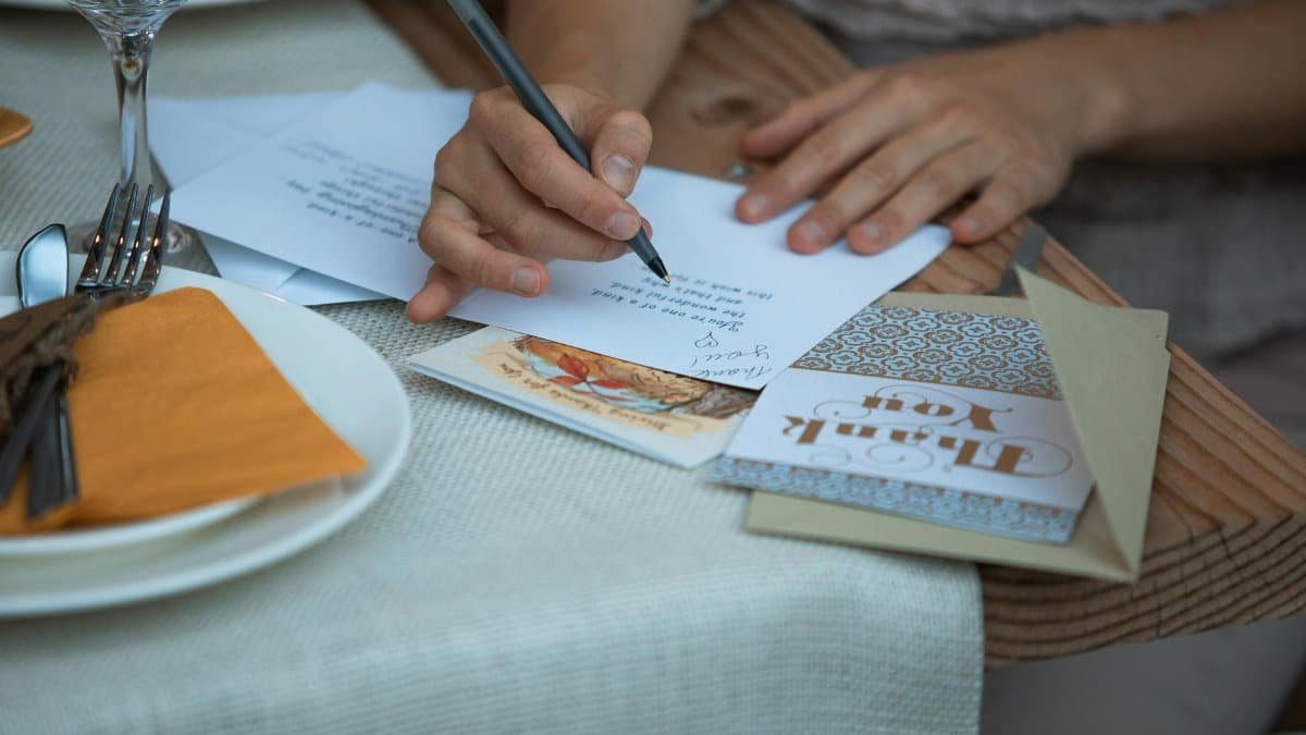 A person writing a Thanksgiving thank you note at a dinner table, surrounded by festive decor.