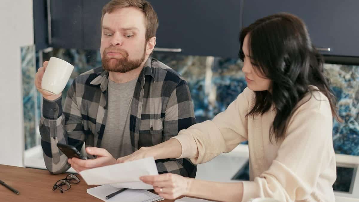 A couple looks worried as they review bills at their kitchen table, reflecting financial concerns.