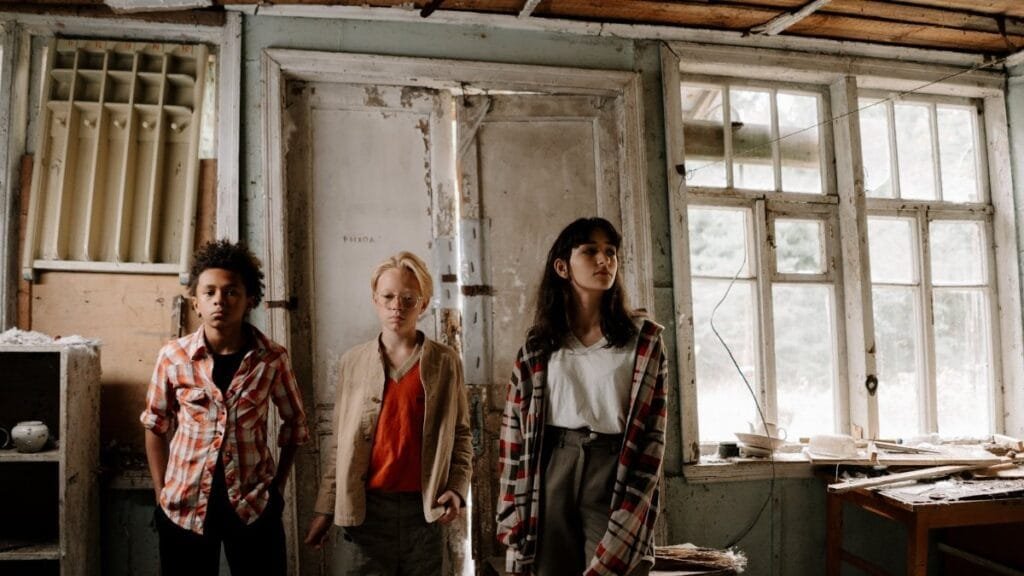 Three teens stand in a shabby, abandoned building for an adventure.