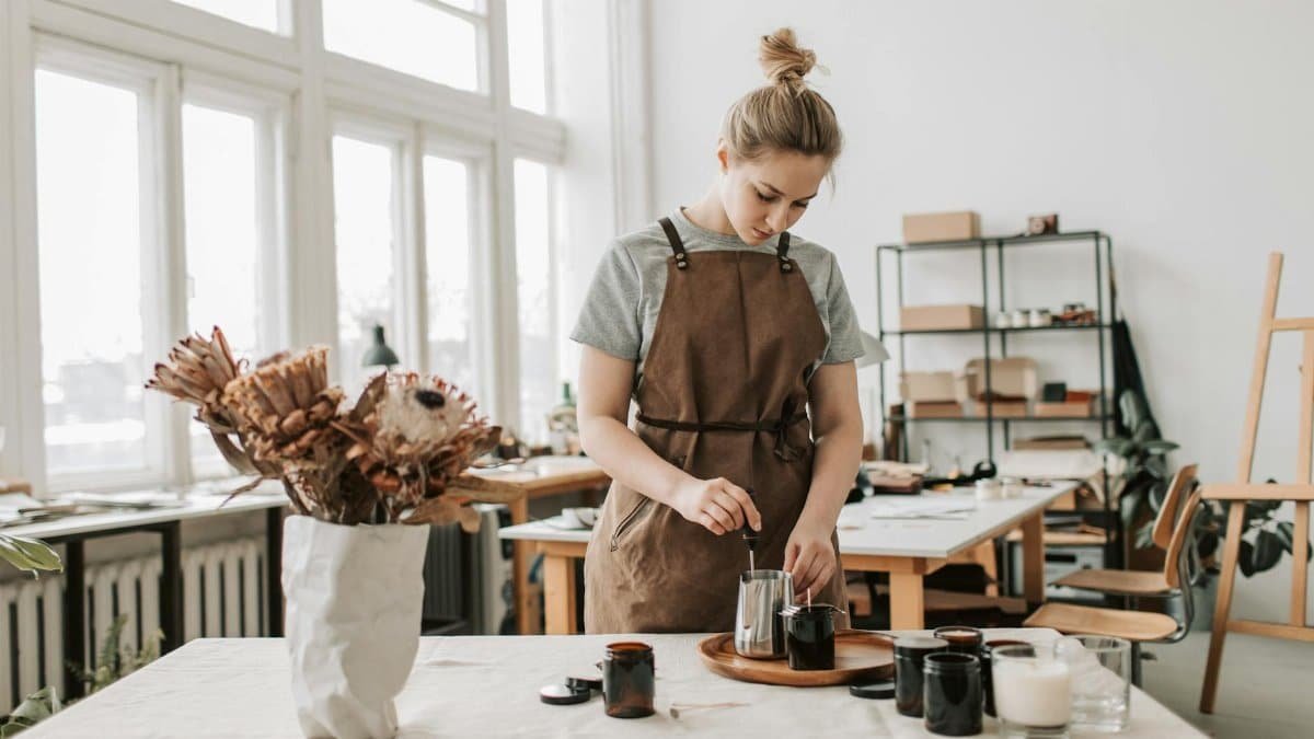 A woman craftsperson creating handmade candles in a bright, airy workshop.