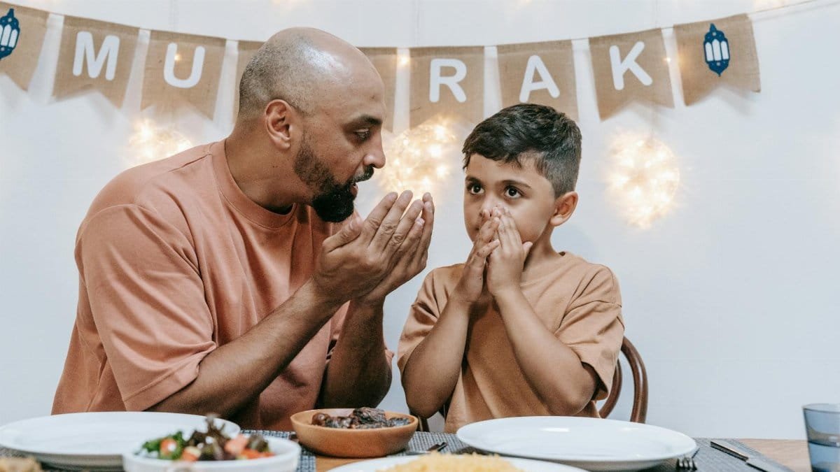 Father and son in prayer before enjoying an Eid meal together at home.