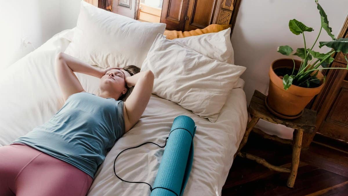 Woman relaxing on bed with yoga mat, enjoying leisure time in a cozy bedroom setting.