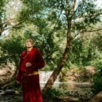 A Buddhist monk stands peacefully in a lush forest near a serene waterfall, embracing nature.
