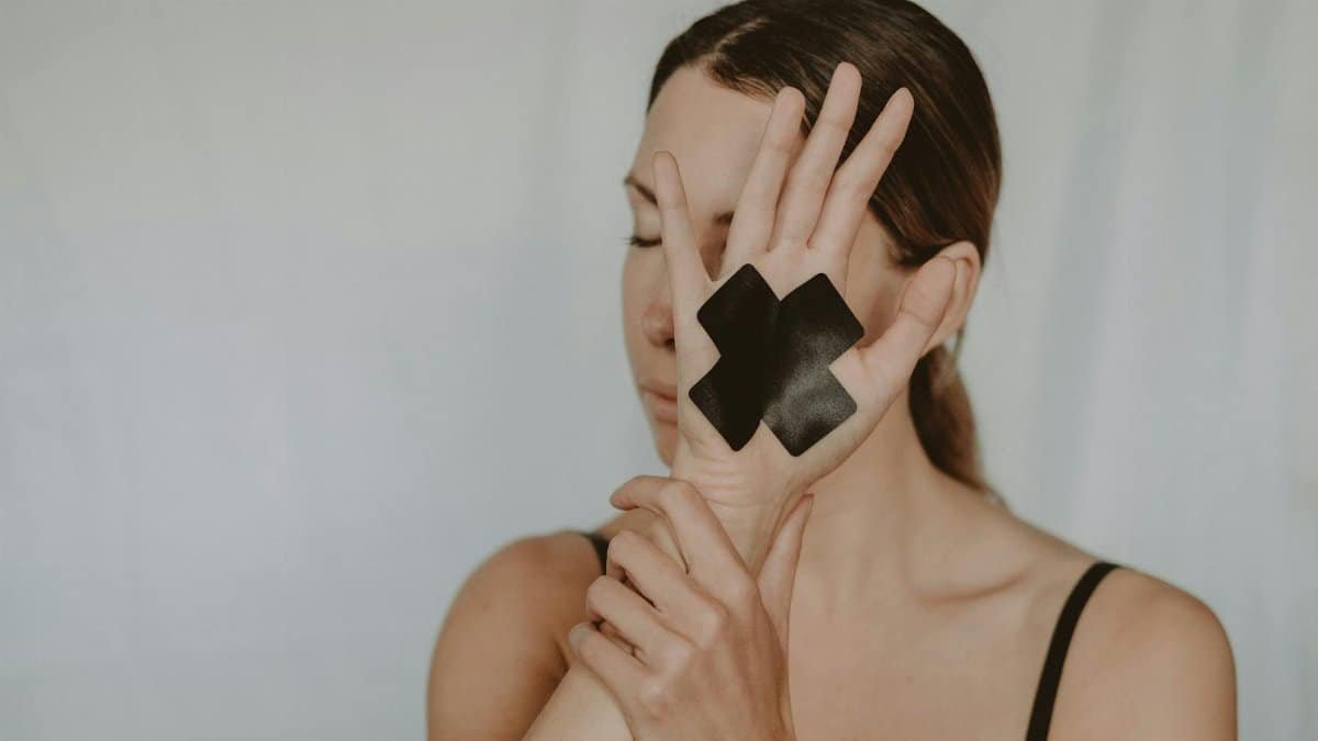 Young woman in black lingerie with closed eyes demonstrating hand with black tape cross against violence on white background