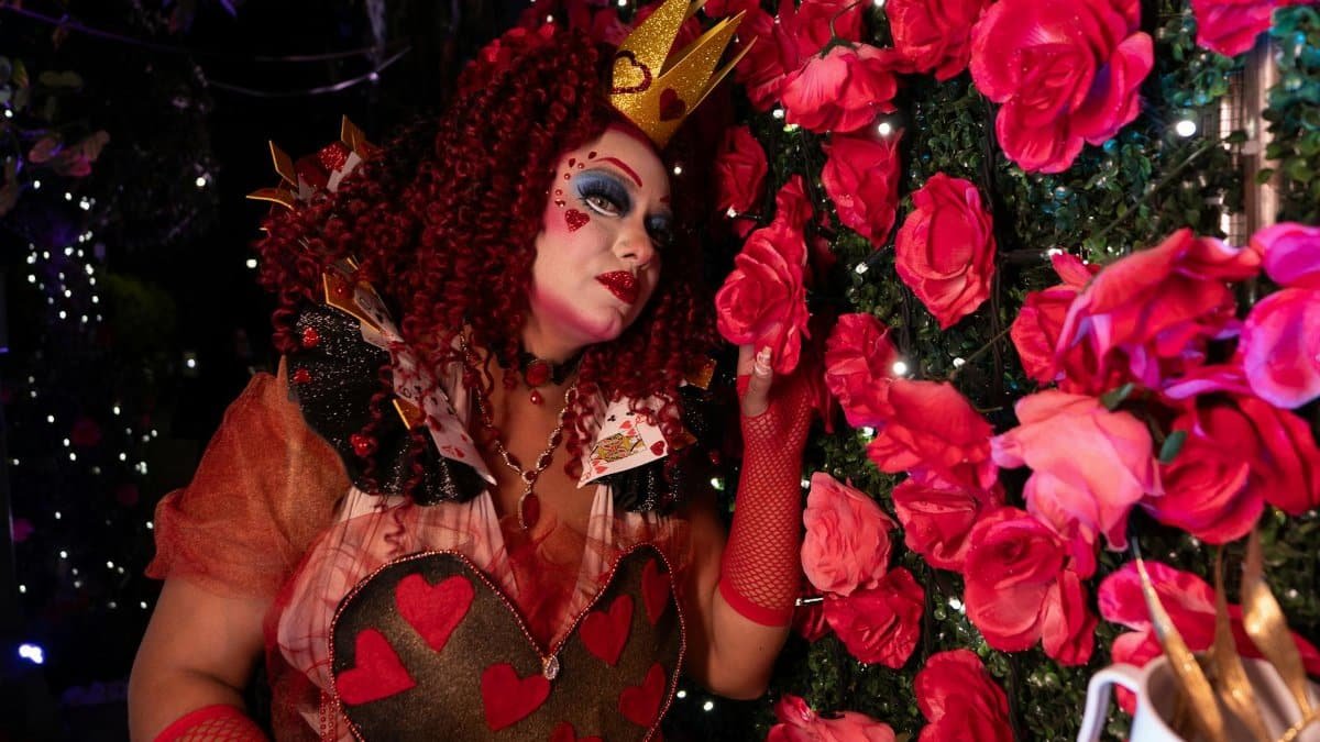 Vibrant Queen of Hearts cosplay amidst a rose garden with intricate artistic makeup.
