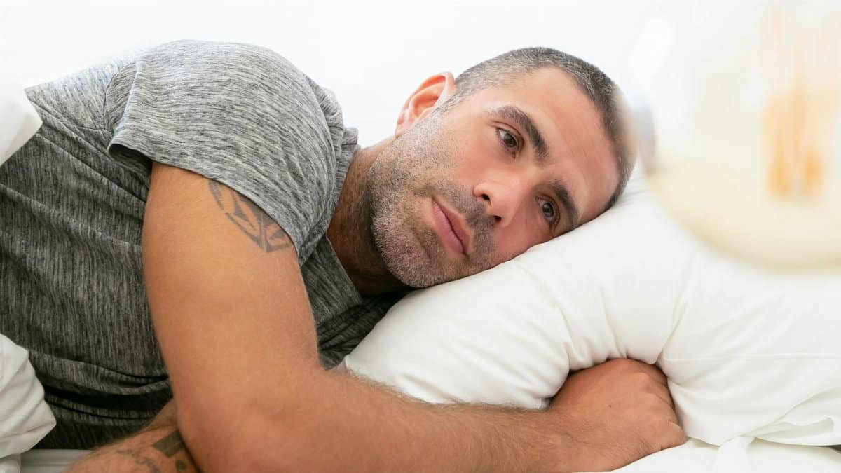 A man in a gray shirt lying on a pillow, reflecting on thoughts.