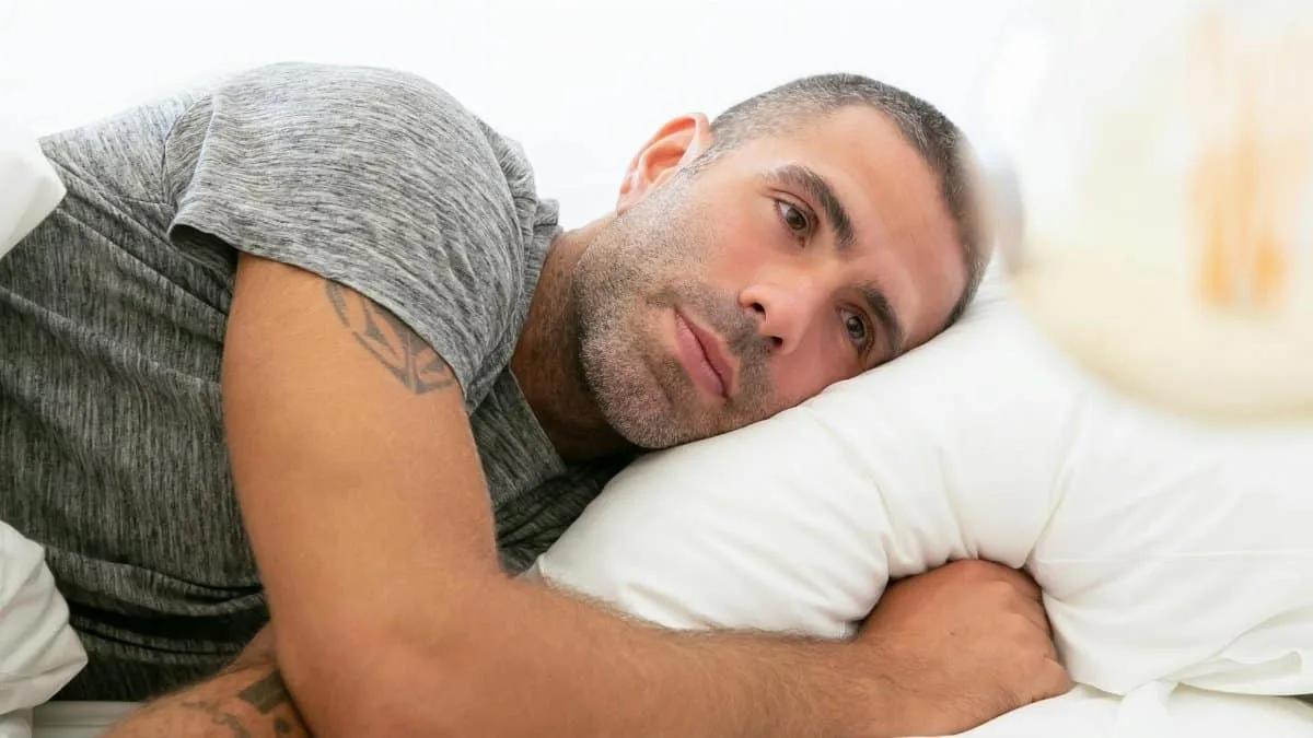 A man in a gray shirt lying on a pillow, reflecting on thoughts.