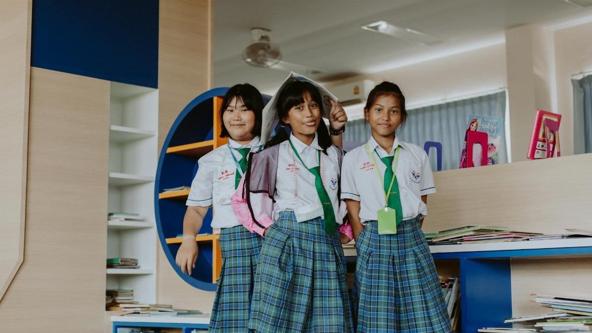 Three schoolgirls in uniform smiling happily while posing inside a library.