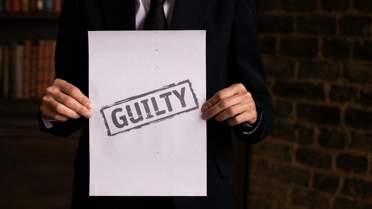 A businessman in a formal suit holding a sign with the word 'GUILTY.'