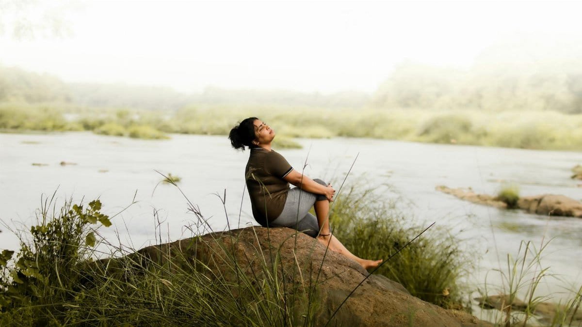 Woman enjoying a peaceful moment by the riverside, embracing nature's serenity.