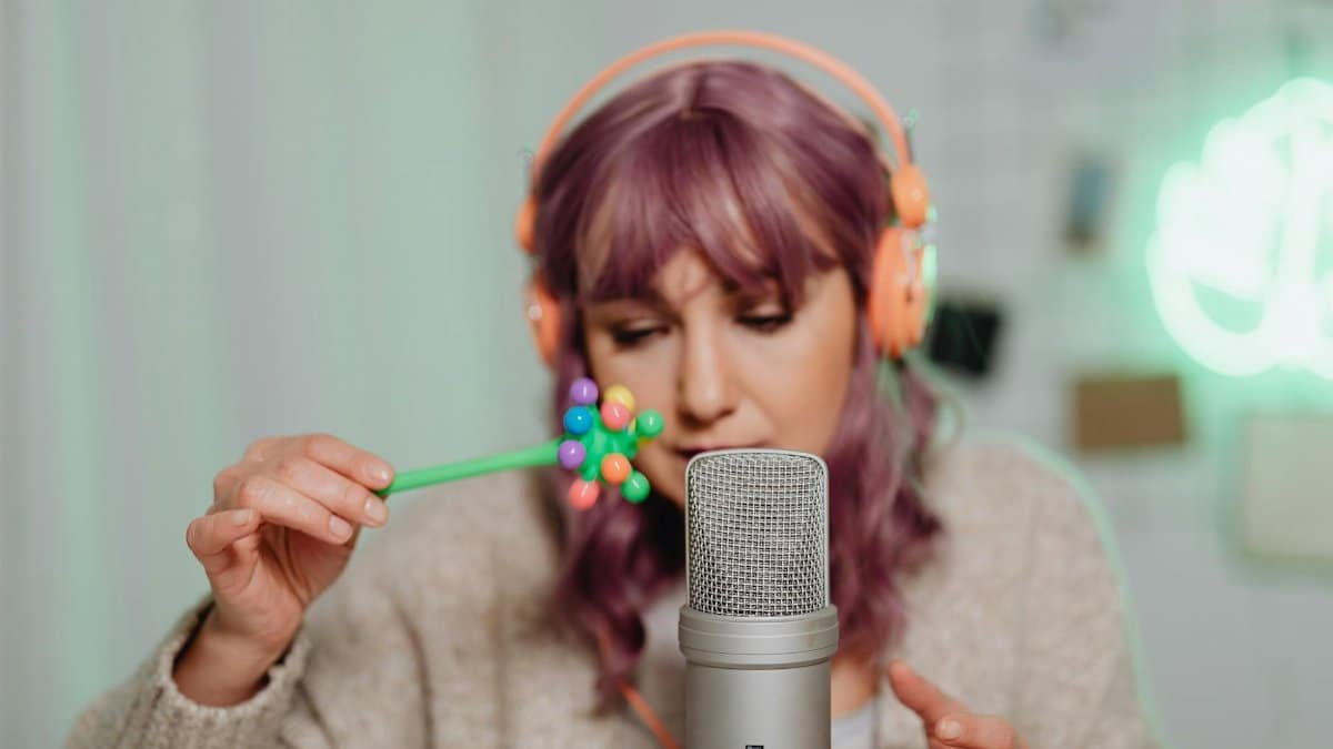 Woman with purple hair recording ASMR using a microphone and colorful props.