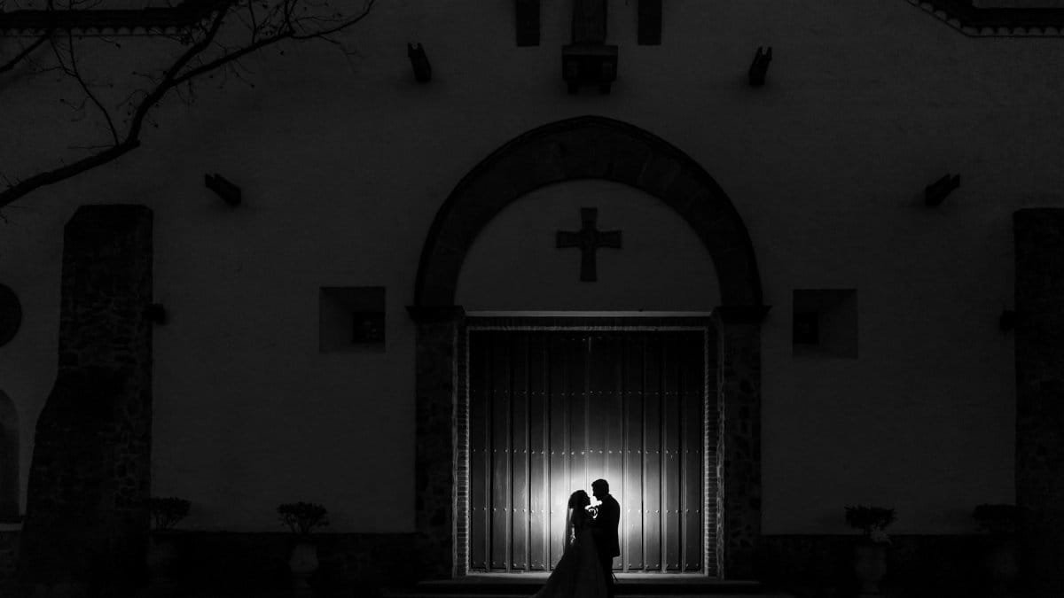 A dramatic black and white silhouette of a newlywed couple outside a church at dusk.