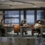 Students studying in a modern library with leather chairs and books around them.