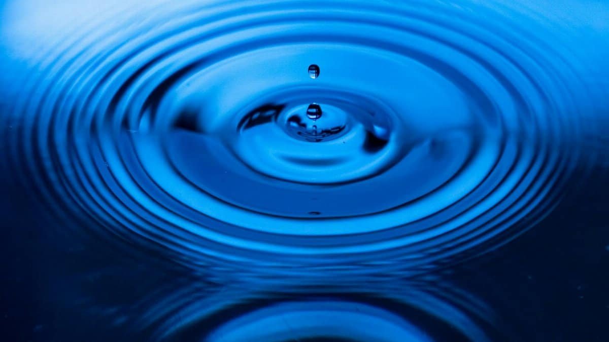 Captivating image of a blue water drop creating ripples on the surface, showcasing nature's beauty.