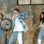 Group of friends dancing indoors with a smartphone and ring light setup for social media content. via Pexels