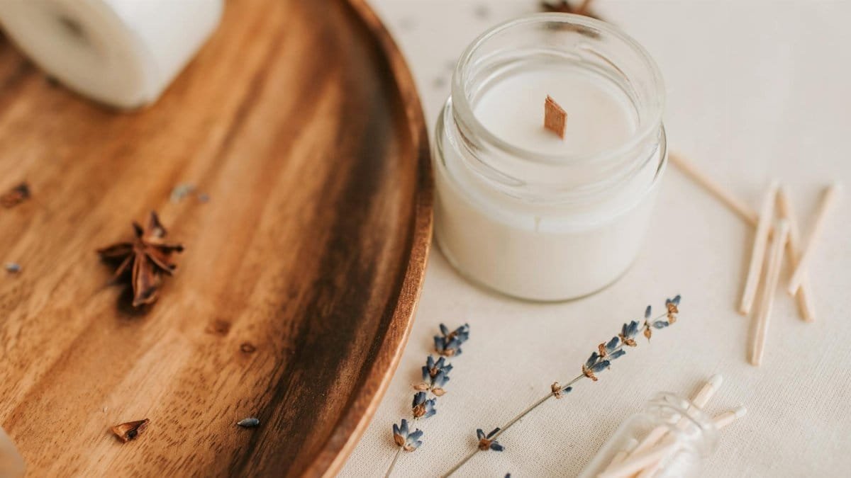 Close-up of a lavender-scented candle in a jar with decor on a wooden tray.