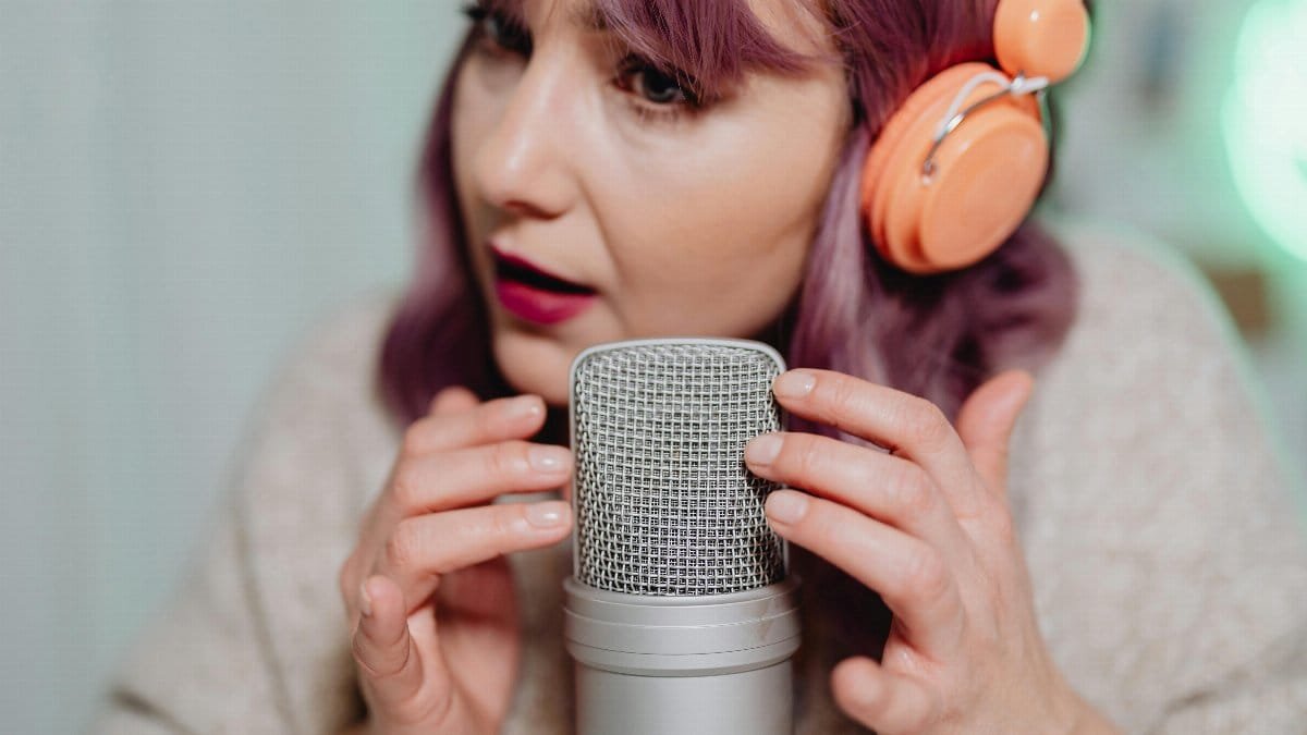 Woman recording ASMR audio with a microphone and headphones in a cozy indoor setting.