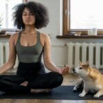 Woman meditating on yoga mat with Shiba Inu dog indoors. Calm and serene home setting.