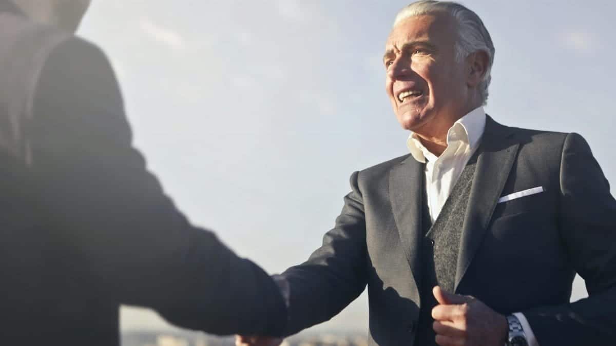 A senior businessman warmly shakes hands outdoors, symbolizing agreement and mutual respect.