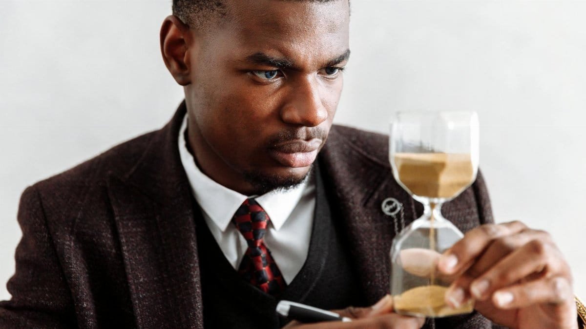 Serious businessman contemplating time with an hourglass, symbolizing focus and management.