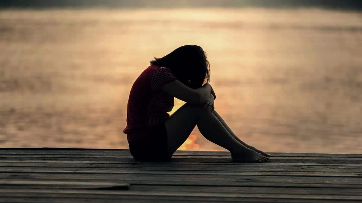 A woman sitting alone on a wooden dock by the lake, showing solitude and reflection.