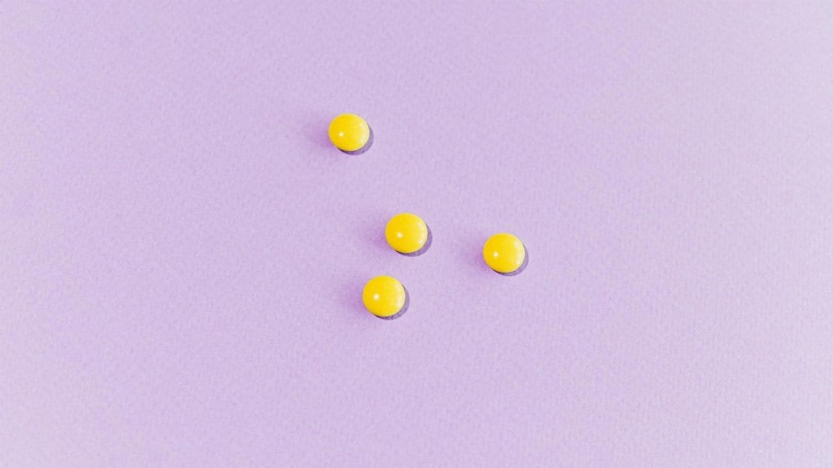 Four yellow pills are arranged on a pastel purple surface, showcasing minimalist design.