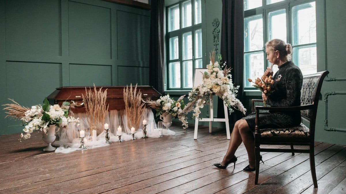 A serene funeral scene with an ornate coffin and floral arrangements indoors, conveying loss and tribute.