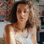 Woman sitting on bed wrapped in a knitted blanket, enjoying a cozy morning sun. via Pexels