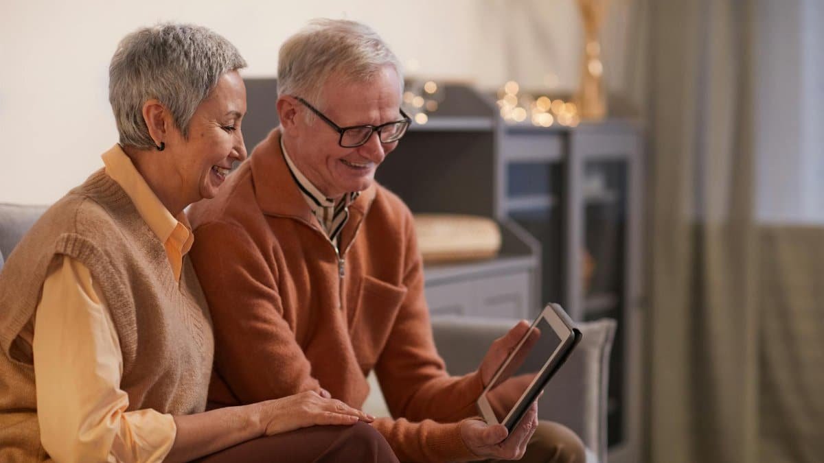 A cheerful senior couple enjoying a video call on a tablet in their cozy living room.