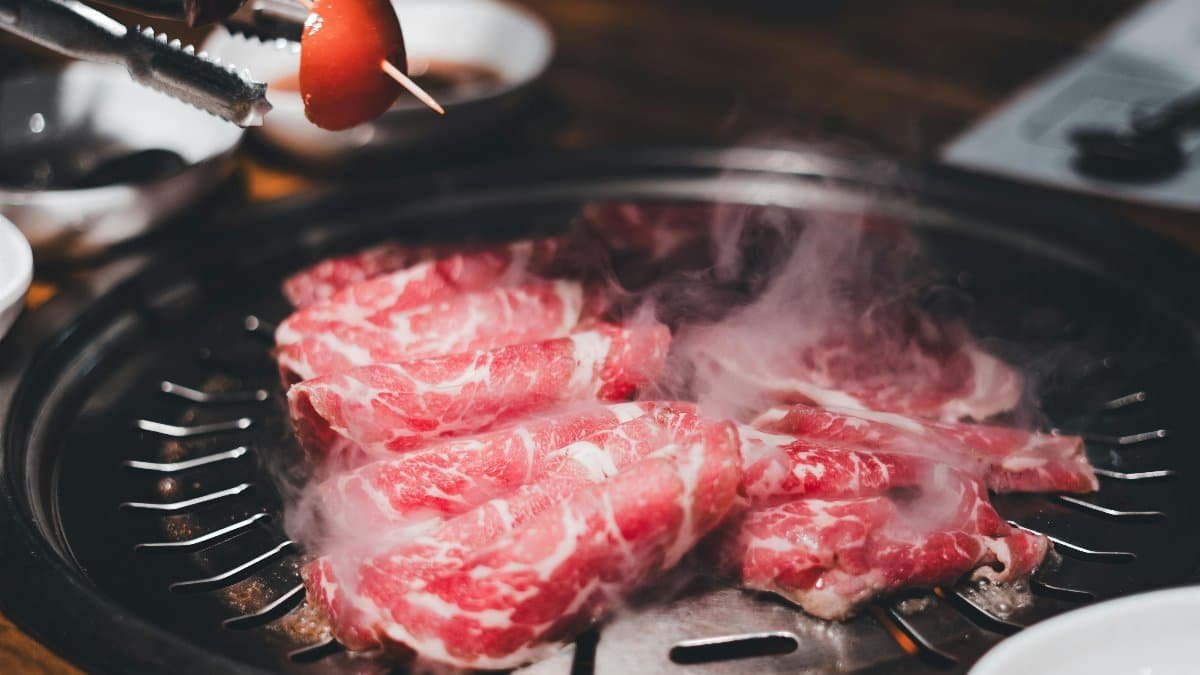 Appetizing grilled meat steaming on an indoor BBQ at a restaurant, with various sides on the table.