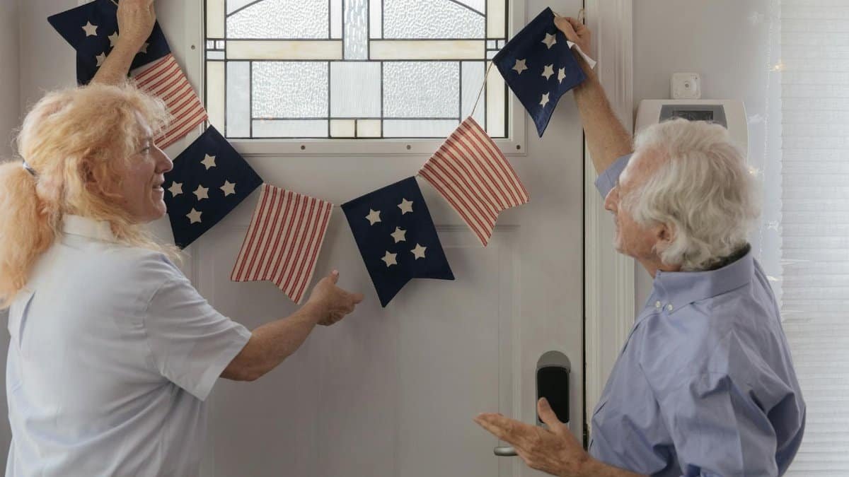 Elderly couple decorates indoors with American flag bunting for a holiday celebration.