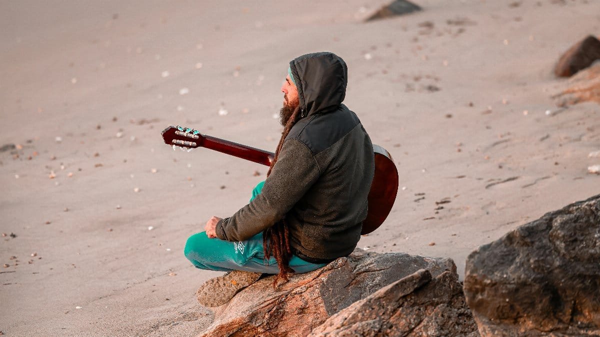 A person sits with a guitar on a sandy beach at dawn, creating a peaceful scene. via Pexels