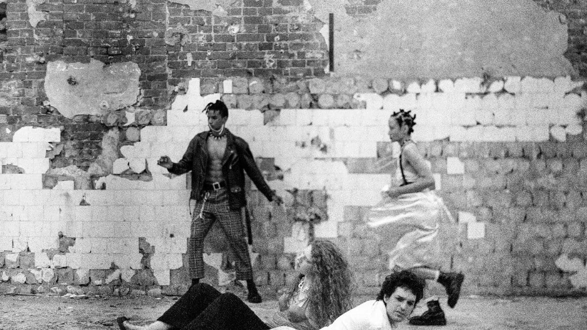 A group of adults posing in a vintage punk fashion set against an abandoned brick wall.