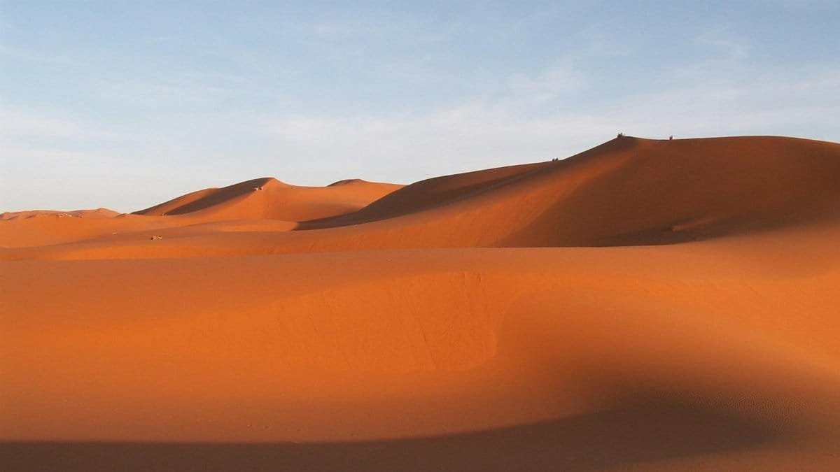 Breathtaking view of orange sand dunes under a clear blue sky, capturing nature's serene beauty.