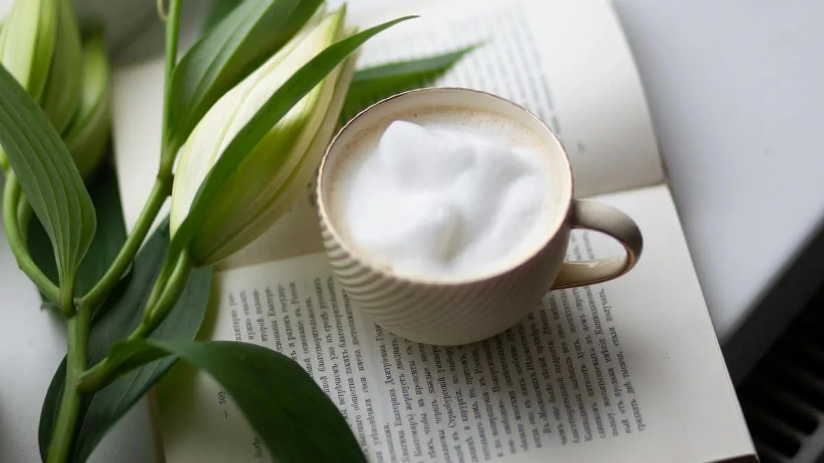 A serene still life of a cappuccino cup, open book, and white lily on a table.
