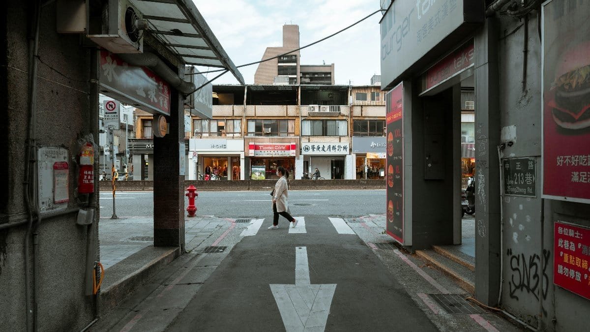 A woman walks across a crosswalk in an urban setting, surrounded by street signs and buildings.