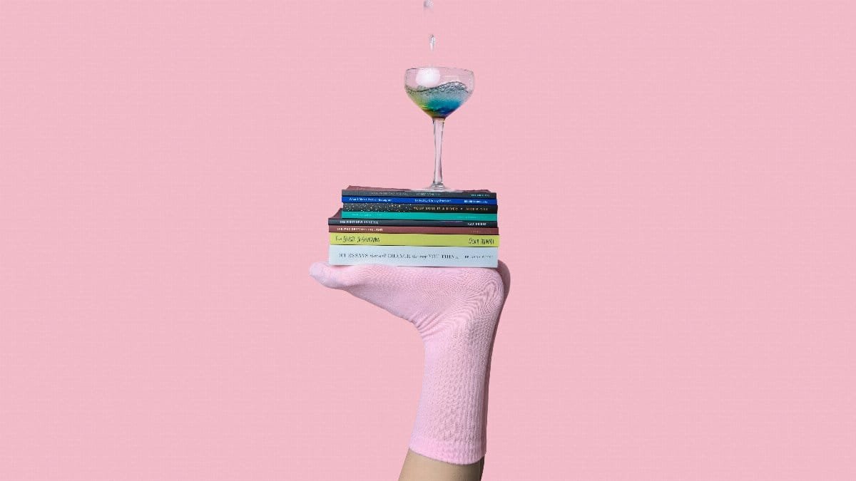 Artistic portrayal of balance using books and a glass on a foot against a pink backdrop.