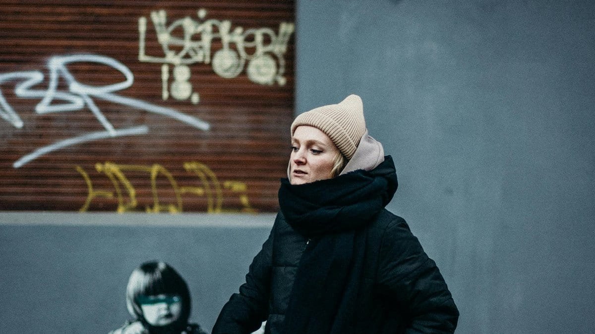 A person walking in a cityscape with graffiti art on the wall, wearing winter attire. via Pexels