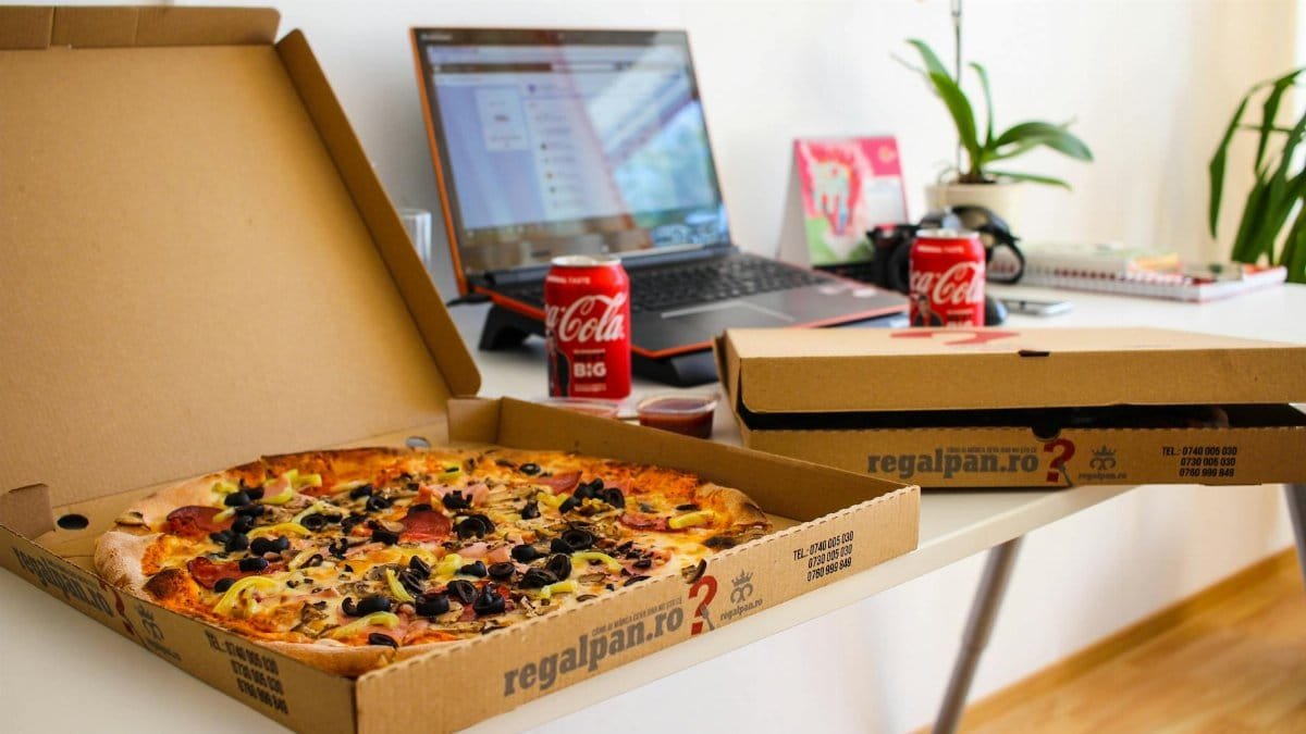 Office workspace with pizza and laptop, showcasing a casual and modern work environment.
