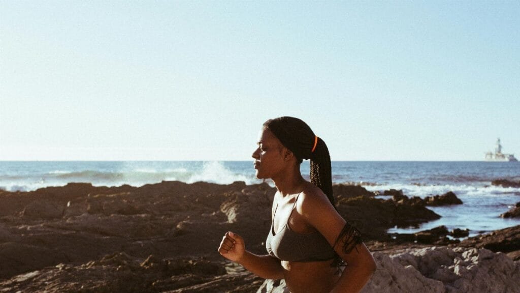 Fit woman running by the ocean, embodying health and wellness outdoors. via Pexels
