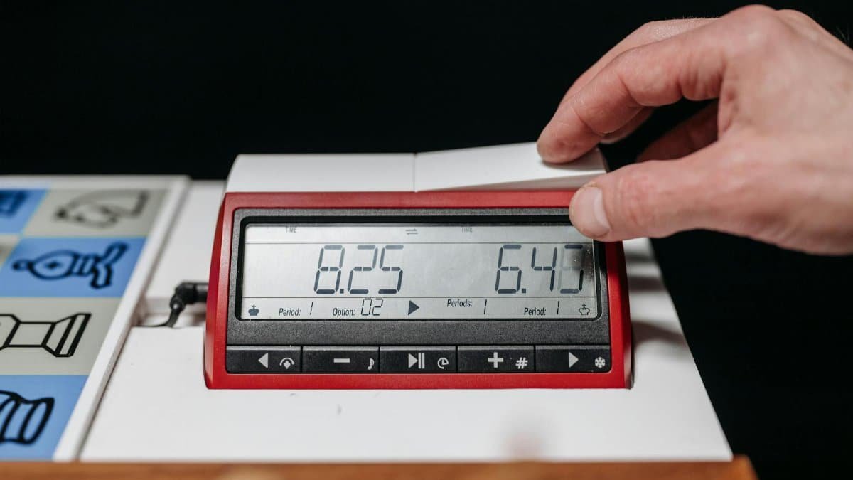 A hand adjusting a digital chess clock during a chess game, close-up shot.