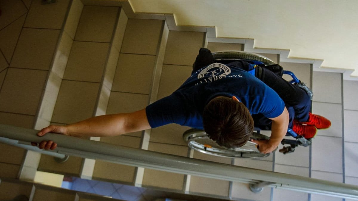 Overhead view of a person in a wheelchair going down stairs indoors, holding onto railings.