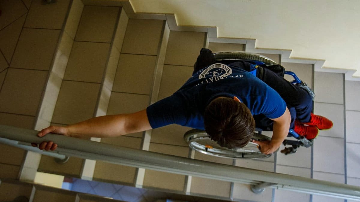 Overhead view of a person in a wheelchair going down stairs indoors, holding onto railings.