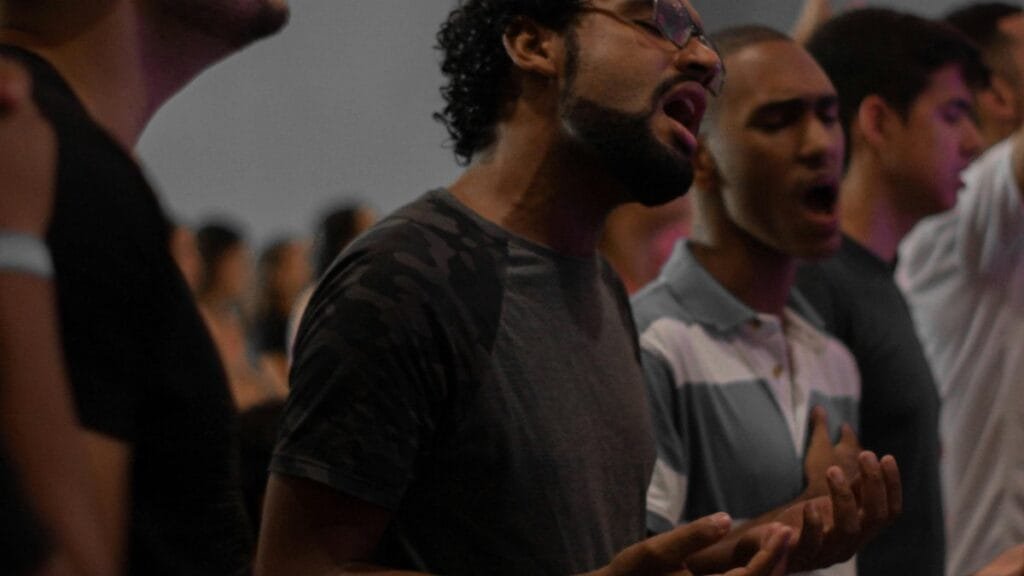 A diverse group of individuals passionately singing and worshiping indoors. via Pexels