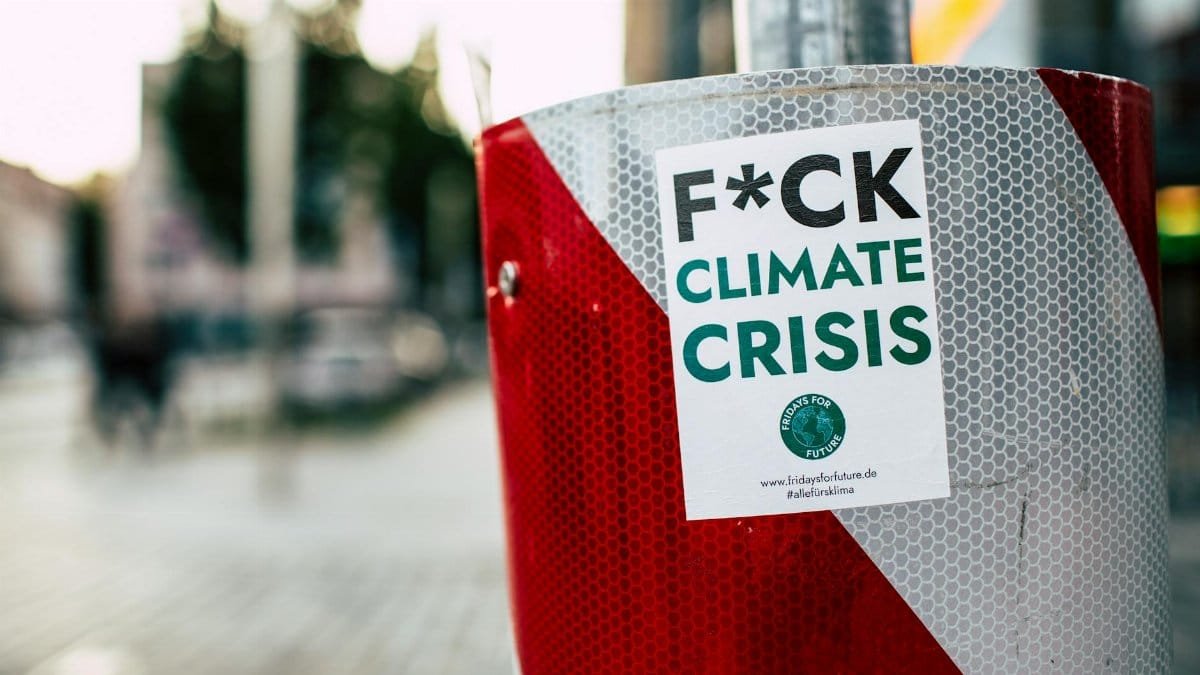 Sticker advocating against climate crisis on a red post in a city street, emphasizing climate action.