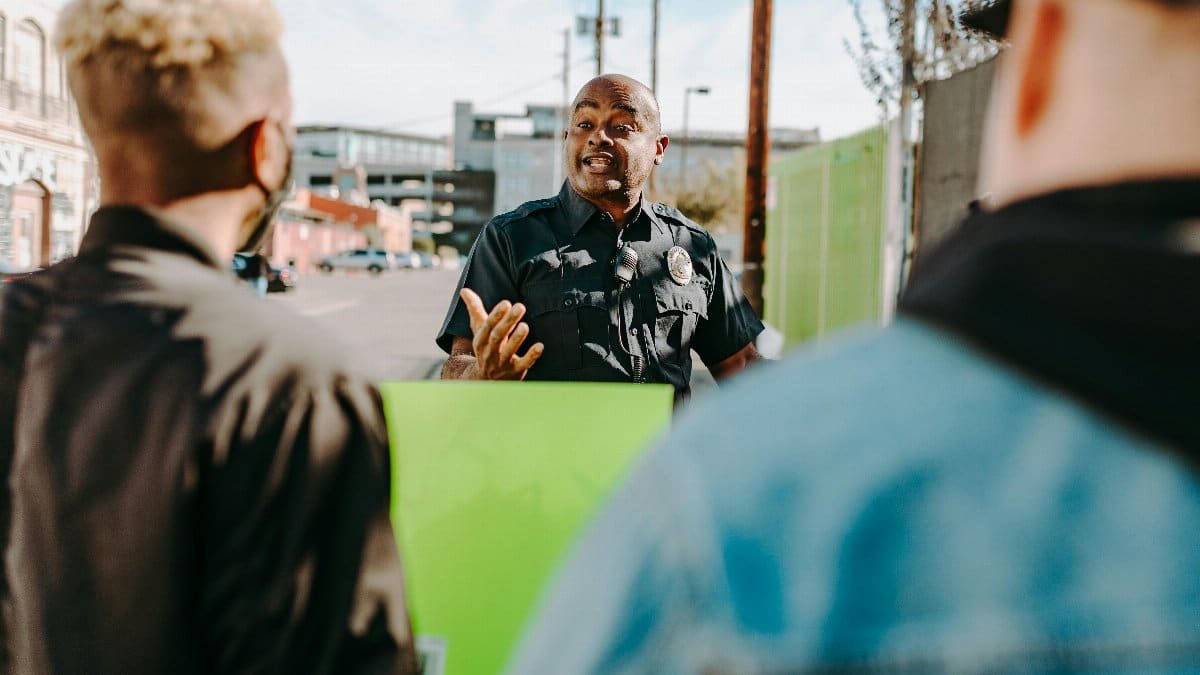 A policeman interacts with protesters holding signs during a daytime city protest.