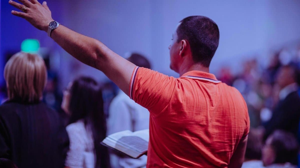 A man worships in a church holding a Bible among a congregation of diverse people.